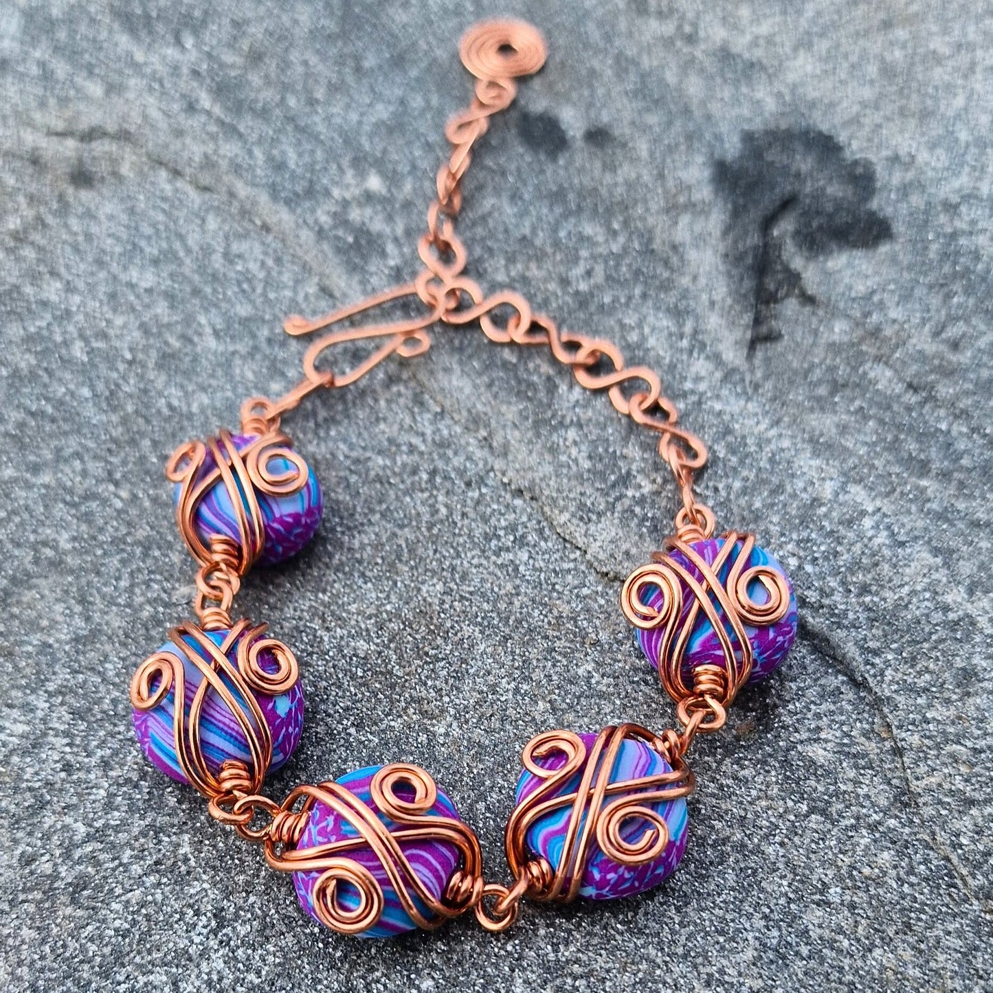 Armbånd med dekorativ kobbertvinning og håndlagde perler i lilla og turkis