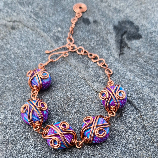 Armbånd med dekorativ kobbertvinning og håndlagde perler i lilla og turkis